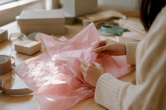 Handen vouwen roze zijdepapier op een houten tafel